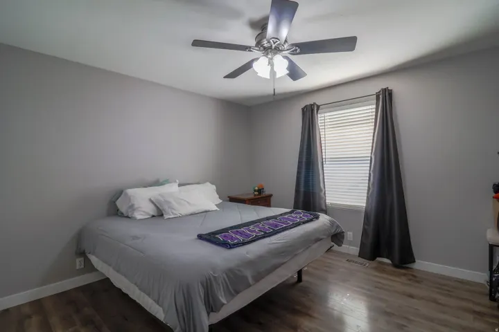Wood-finish flooring, neutral wall paint, ceiling fan with integrated lighting, window with horizontal blinds, and dark drapery panels