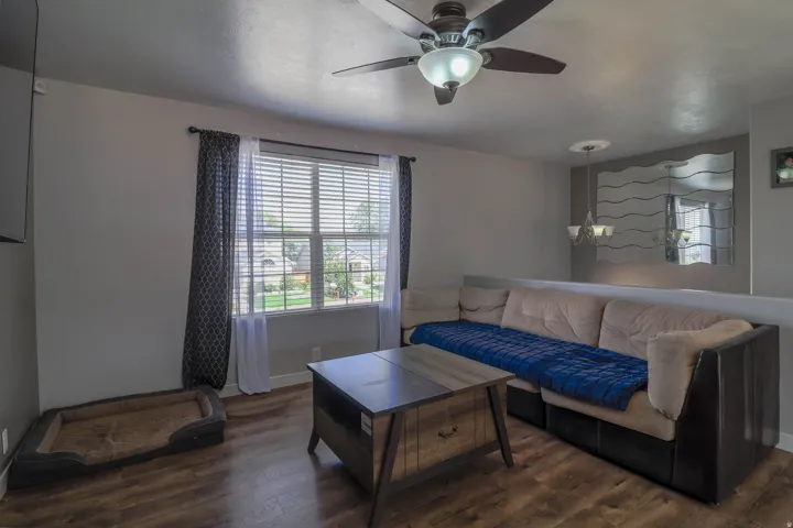 Wood-finish flooring, ceiling fan with integrated lighting, window with blinds, and built-in partial wall