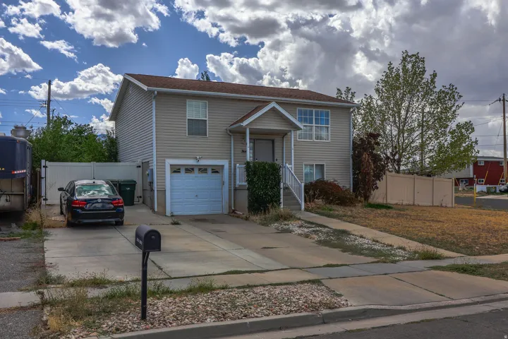 Two-story residence with light-toned siding, attached single-car garage, front porch with white railings, and a concrete driveway