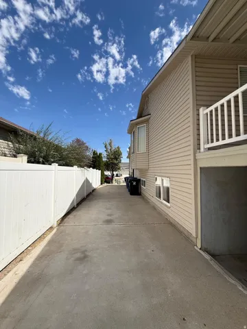 Concrete driveway, vinyl siding exterior, white vinyl fencing, lower-level garage access, and an upper-level balcony