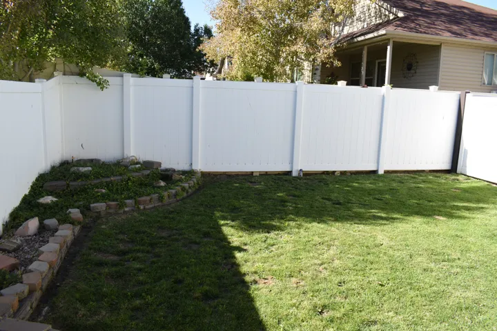 White privacy fencing with a grass lawn and a stone-edged garden bed