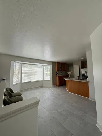 Recessed lighting, light gray tile flooring, bay windows, wood cabinetry, and a kitchen island with a built-in sink
