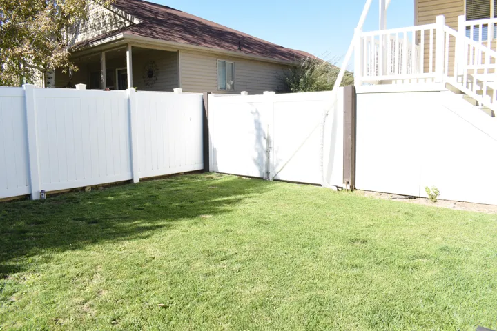 Expansive grassy yard area featuring white panel fencing and a white deck with stairs