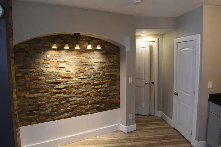 Stacked stone accent wall with arched alcove, integrated four-light fixture, wood-finish flooring, and white paneled doors