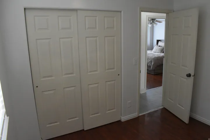 Bi-fold closet doors, wood-finish flooring, white trim, paneled interior door, and light gray wall paint