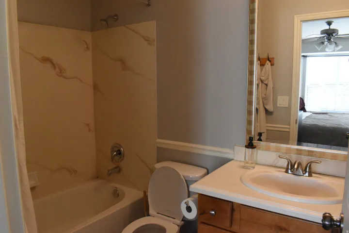 Bathroom featuring a built-in bathtub with a tile surround, a single vanity with a white countertop and undermount sink, and a framed mirror