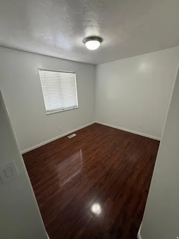Wood-finish flooring with a flush-mount ceiling light fixture, window with horizontal blinds, and light-toned wall paint