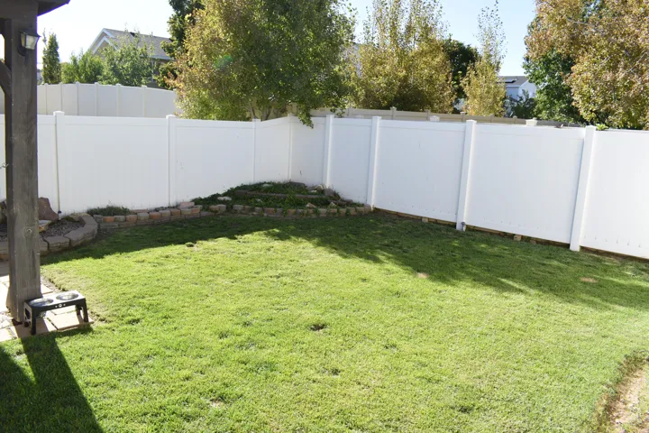 Expansive lawn area with a white privacy fence and a stone-edged garden bed