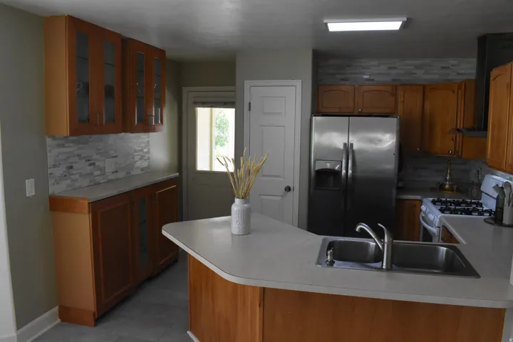 Kitchen featuring wood-finish cabinetry, a stainless steel refrigerator, a built-in range, mosaic tile backsplash, and a counter-height island with an undermount sink