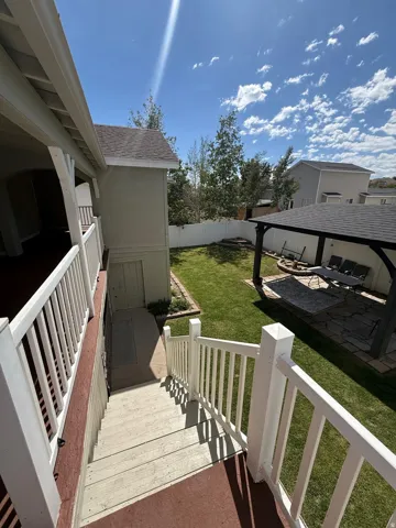Expansive backyard featuring a manicured lawn, white privacy fence, covered patio with stone pavers, and a dedicated basement entrance
