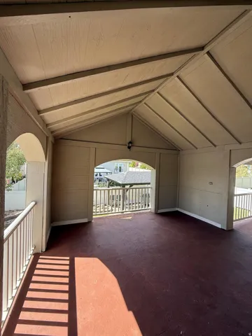 Covered patio with a gabled ceiling, painted wood railings, and a red-toned floor surface