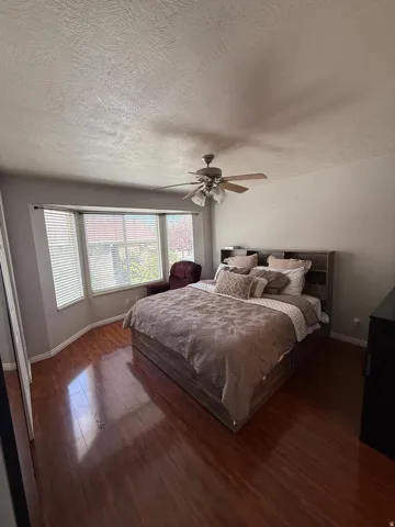 Bay window with horizontal blinds, wood-finish flooring, and a ceiling fan with light fixture