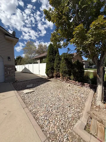 Stone landscaping with brick edging, concrete driveway, and white privacy fencing