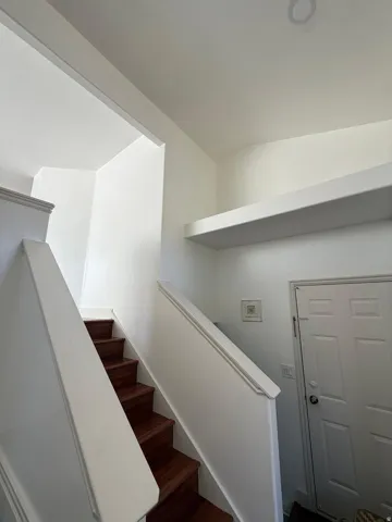 Wood-finish stairs with white risers and railings, complemented by white walls and a recessed ceiling light