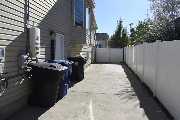 Side yard with concrete paving, fully fenced perimeter, and a utility access door