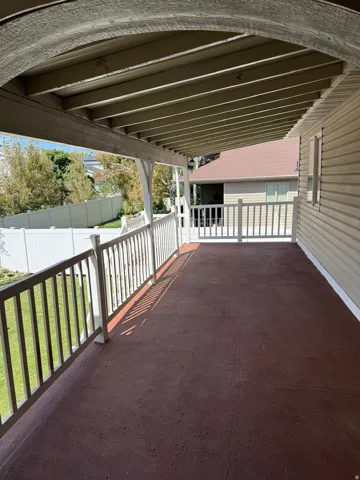 Covered outdoor patio with a textured surface, white railing, and exterior siding