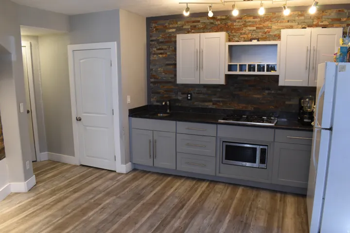 Kitchenette featuring wood-finish flooring, grey cabinetry, a stone-tiled backsplash, dark countertops, and track lighting