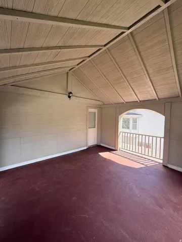 Covered patio with a high vaulted ceiling, red-toned floor, and an exterior door