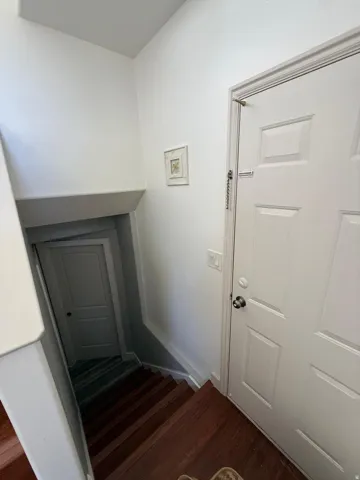 White paneled door with a privacy lock, wood-finish flooring, and white painted walls