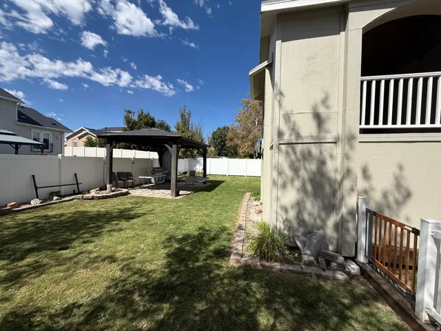 Expansive backyard featuring a spacious lawn, white vinyl fencing, a paved patio with a dark wood-finish pergola, and a second-story balcony with white railings