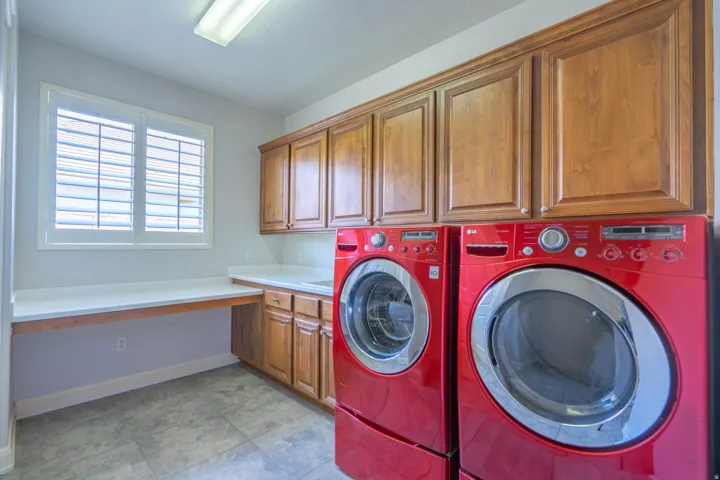 Laundry room featuring a built-in sink, upper and lower wood cabinetry, a window with plantation shutters, and light-toned tile flooring