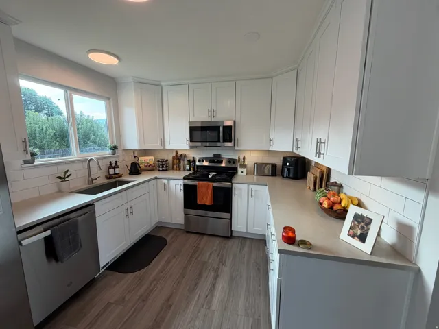 White shaker cabinetry, stainless steel appliances, wood-finish flooring, subway tile backsplash, and light-toned countertops