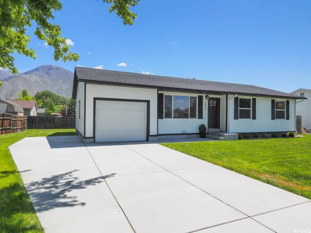 White exterior with black trim, attached garage, concrete driveway, and a manicured lawn