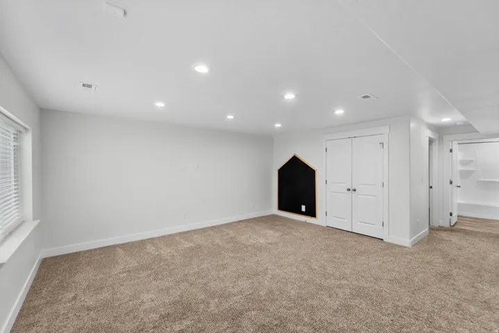 Fun and functional basement bedroom perfect for kids, featuring a creative chalkboard wall ideal for drawing, learning, and imaginative play. Bright recessed lighting illuminates the space, while neutral wall paint provides a clean, versatile backdrop tha