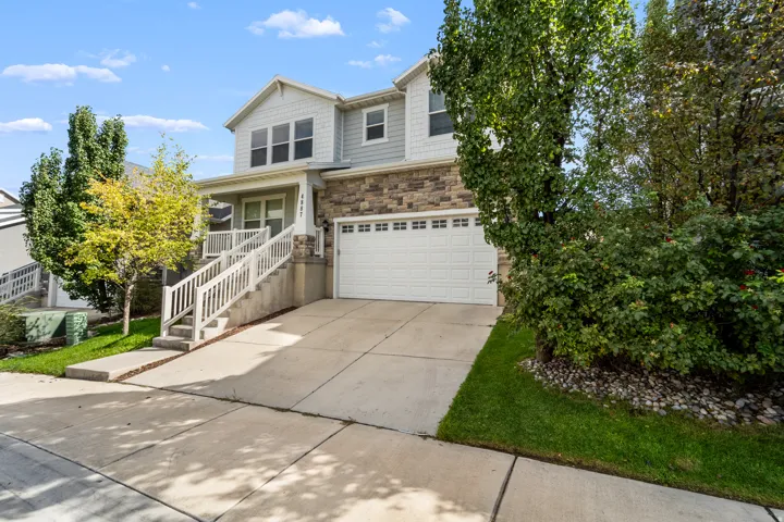 Two-story exterior with stone and siding facade, covered entry porch, white garage door, and concrete driveway