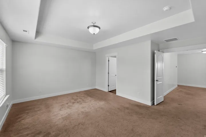 Stunning master bedroom featuring an impressive double door entry that sets an elegant tone for this expansive suite. Dramatic tray ceilings command attention and create a sense of luxury and openness, while calming neutral wall paint establishes a peacef