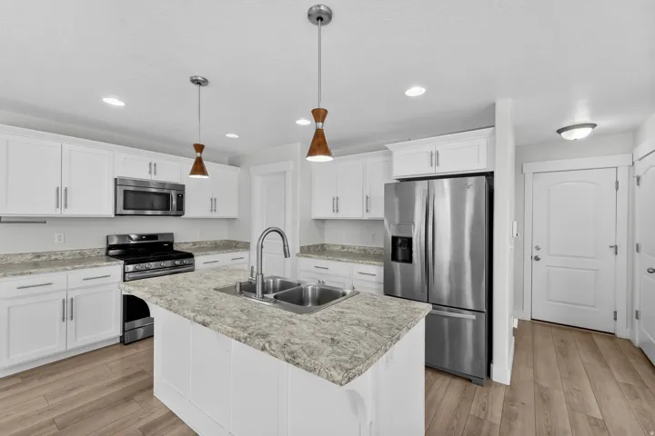 Attractive kitchen showcasing clean white cabinetry and quality stainless steel appliances for a contemporary aesthetic. The centerpiece kitchen island with dual-basin sink enhances both functionality and style, while beautiful wood-finish flooring adds w