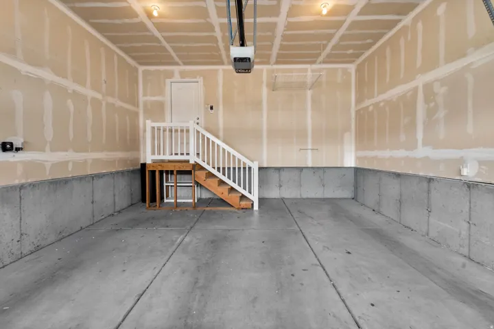 Large, functional garage with sturdy concrete flooring designed for durability and easy maintenance. The unfinished drywall offers a blank canvas for future customization, while the convenient interior access door with staircase creates seamless flow to t