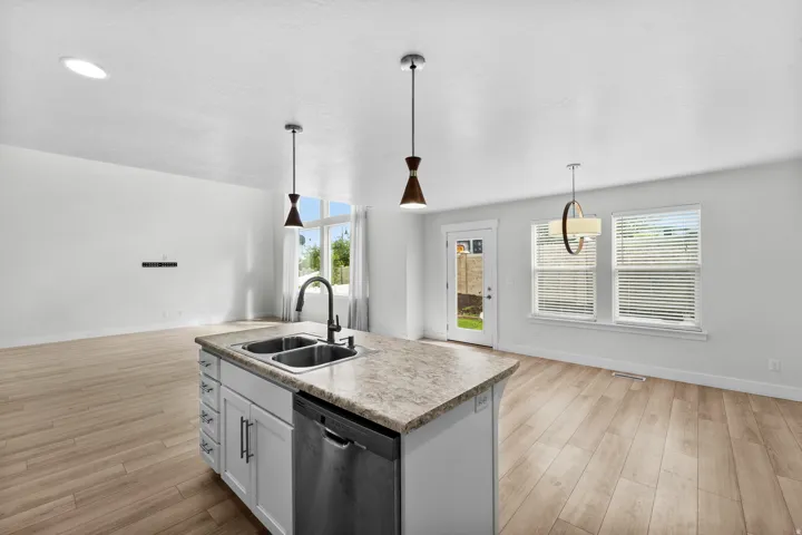 Inviting open-concept kitchen connected to dining and living spaces, perfectly designed for modern entertaining. The centerpiece kitchen island features a practical double basin sink, complemented by a stainless steel dishwasher and elegant pendant lighti