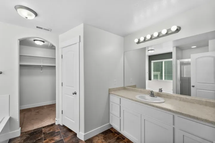 Elegant master bathroom featuring a pristine white cabinetry vanity with generous storage and functionality. A generously sized mirror reflects light throughout the space, while a sophisticated multi-bulb light fixture delivers bright, even illumination f