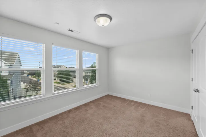 Bright and airy secondary bedroom featuring an impressive triple window array that floods the space with natural light and offers beautiful views. Serene neutral wall color creates a calm, versatile backdrop perfect for any décor style. Recessed lighting