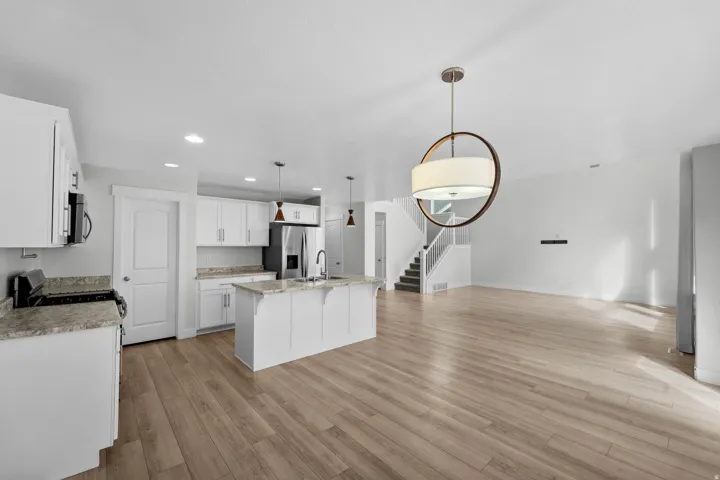 Gorgeous open-concept living space showcasing quality wood-finish flooring that anchors the entire area. Bright white cabinetry creates a fresh, clean aesthetic with excellent storage and display opportunities. The cohesive design flows beautifully, makin