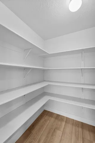 Well-designed kitchen showcasing custom wraparound shelving offering ample storage and display space for cookware and serveware. The warm wood-finish flooring adds warmth and character, complemented by bright overhead lighting that creates an inviting, fu