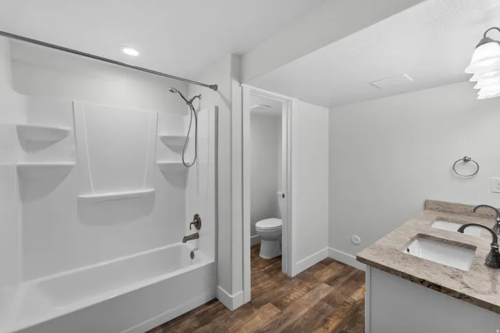 Spacious basement bathroom showcasing a practical dual vanity offering excellent functionality for busy households. Beautiful wood-finish flooring complements the fresh aesthetic, while a stylish white tub and shower combination provides flexibility for d