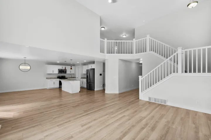 Breathtaking open living area defined by elegant vaulted ceilings that create dramatic architectural interest and abundant natural light. An upper-level balcony overlooks the space, adding dimension and visual flow between levels. Light wood-finish floori