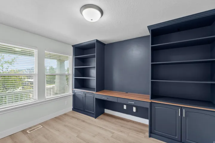 Professional home office showcasing custom cabinetry tailored to this residence. Display-ready open shelving and practical lower storage cabinets in elegant navy finish complement a quality wood-finish work surface. Integrated power outlets provide conven
