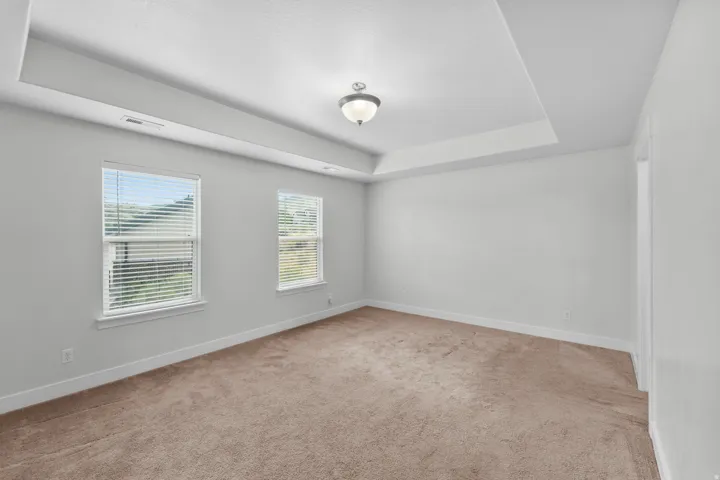 Luxurious master bedroom featuring a sophisticated recessed ceiling that creates clean, modern lines and a streamlined aesthetic. A central flush mount light fixture provides bright, even illumination throughout the room, ensuring excellent lighting for d