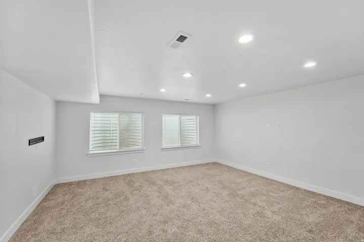 Spacious basement great room flooded with natural light from two windows and enhanced by recessed lighting for an airy, welcoming feel. Soft carpeted flooring creates a comfortable environment, while a stylish staircase with white railings seamlessly conn