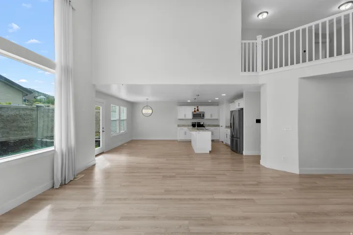 Breathtaking open living area defined by elegant vaulted ceilings that create dramatic architectural interest and abundant natural light. An upper-level balcony overlooks the space, adding dimension and visual flow between levels. Light wood-finish floori
