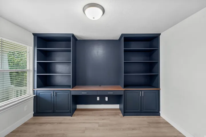 Professional home office showcasing custom cabinetry tailored to this residence. Display-ready open shelving and practical lower storage cabinets in elegant navy finish complement a quality wood-finish work surface. Integrated power outlets provide conven