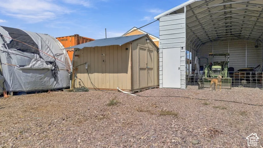 Corrugated metal storage shed, wood-sided storage shed, gravel ground cover, and metal-framed structure