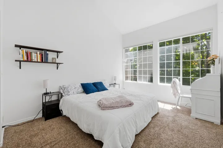 Vaulted ceiling enhancing vertical space, large multi-pane windows, built-in shelving, and carpeted flooring