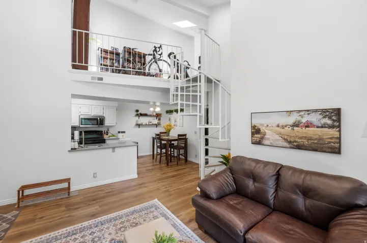 Vaulted ceilings with a skylight, loft area with metal railing, spiral staircase, wood-finish flooring, and a kitchen with white cabinetry and stainless steel appliances