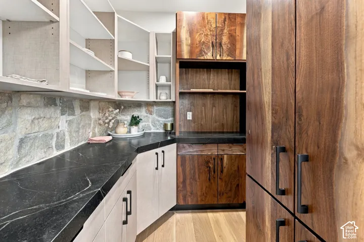 Custom cabinetry featuring light and rich wood-finish doors, dark stone countertops, natural stone backsplash, and matte black hardware