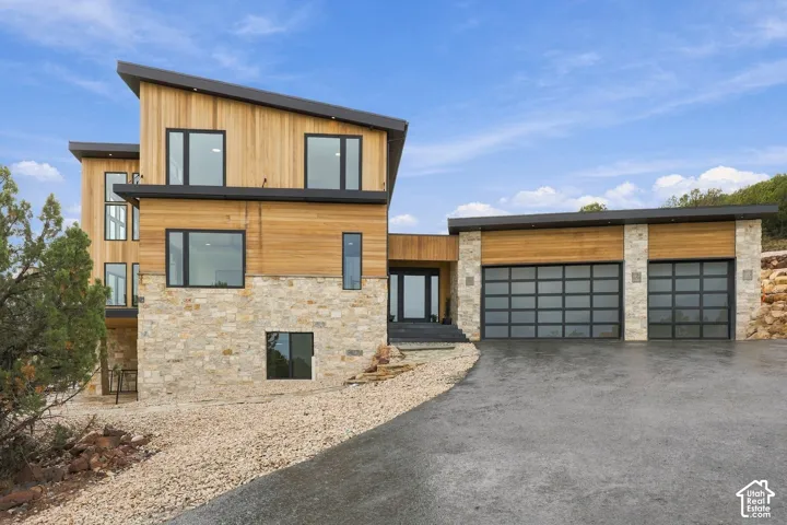 Modern architectural exterior featuring wood-plank siding, multi-tonal stone masonry, a shed-style roof, and a two-car garage with frosted glass panel doors