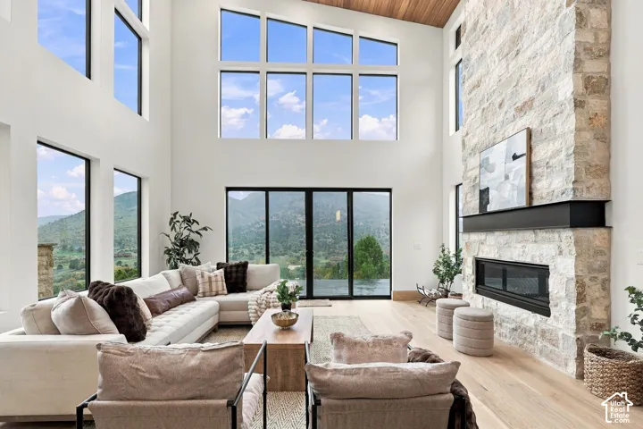 Double-height living area featuring floor-to-ceiling windows, full-height natural stone fireplace, wood-plank ceiling treatment, and wide-plank wood-finish flooring